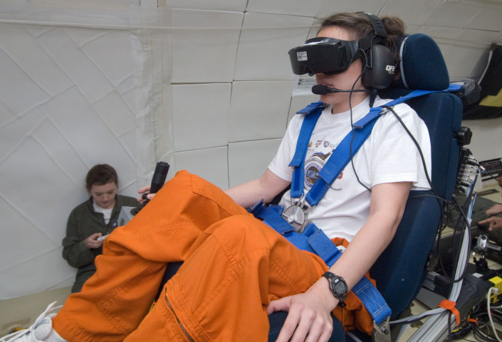 Kara Beaton, seated in the experiment’s tilted chair, performed the virtual navigation task with and without the help of the tactile cueing of her orientation. Kate Montgomery, seated on floor, operates the experiment. Photo by NASA.